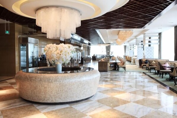 A hotel lobby with a round marble reception desk, a large chandelier, and a check-in counter.