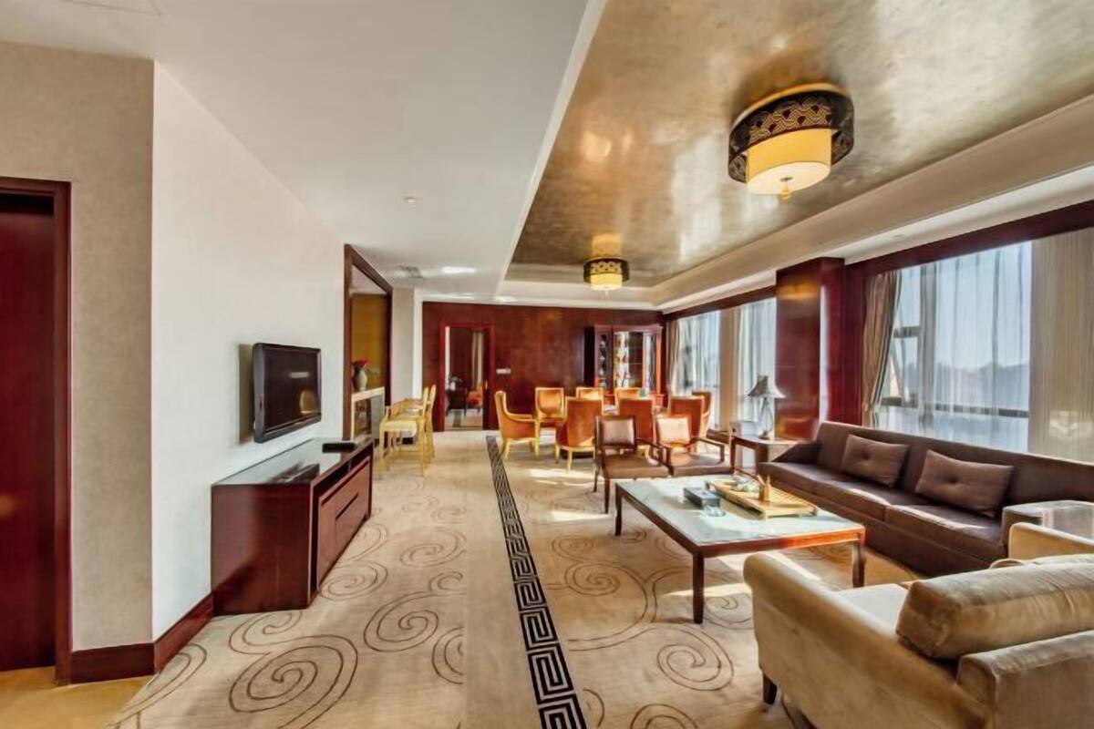 A hotel room with a sofa, a dining area, and a TV.