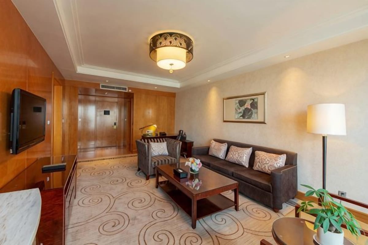 A hotel lobby with a sofa, a coffee table, a television, a lamp, and a patterned carpet.
