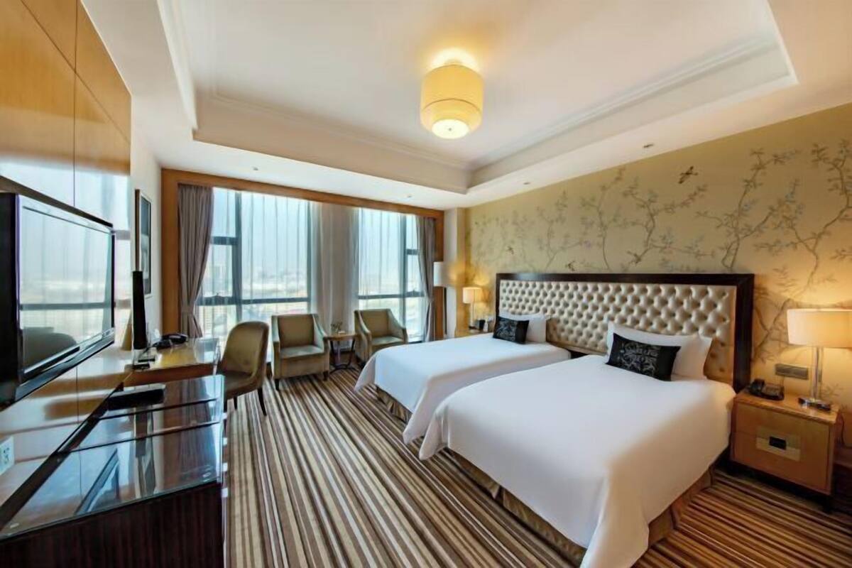 A hotel room with two beds, a desk, a TV, and a large window.