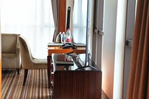 Quarto de hotel com cama, escrivaninha, cadeira e janela.