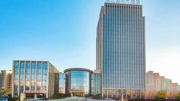 A modern high-rise building with a glass facade, surrounded by other buildings and a clear sky.