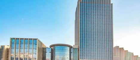 Un moderno edificio de gran altura con fachada de vidrio, rodeado de otros edificios y un cielo despejado.