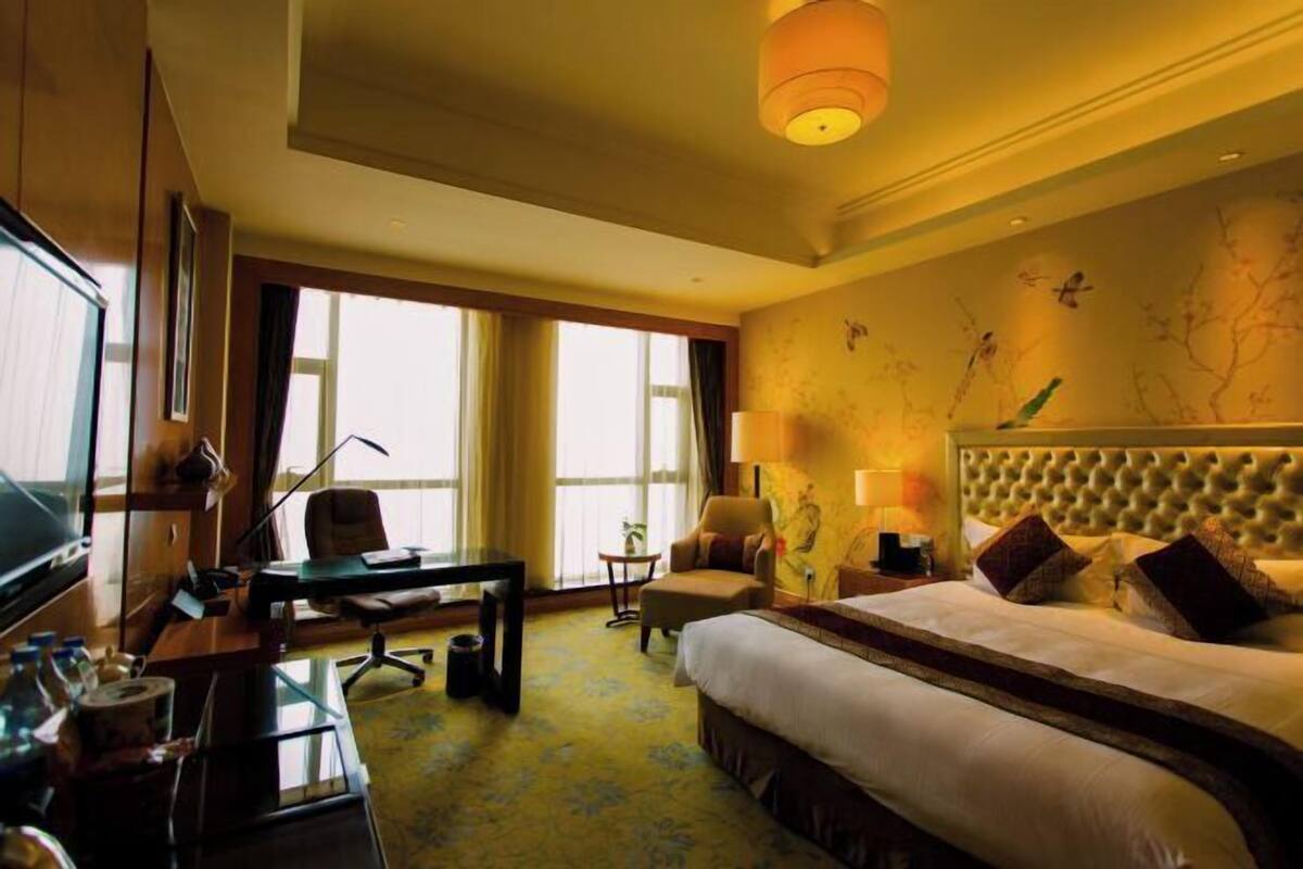 A hotel room with a large bed, a desk, a chair, a television, and a window with curtains.