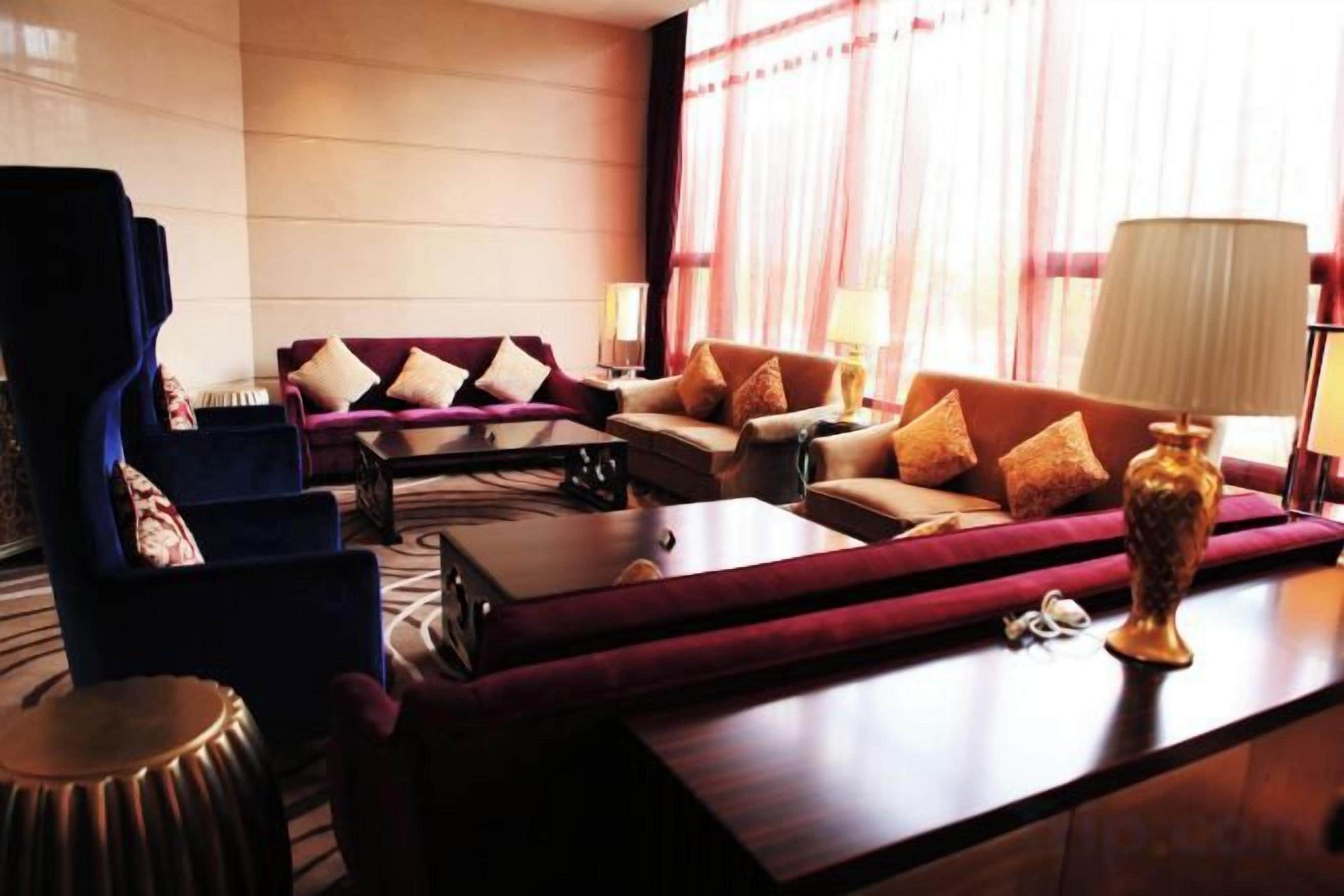 A hotel lobby with a sofa set, armchairs, a coffee table, and a lamp.