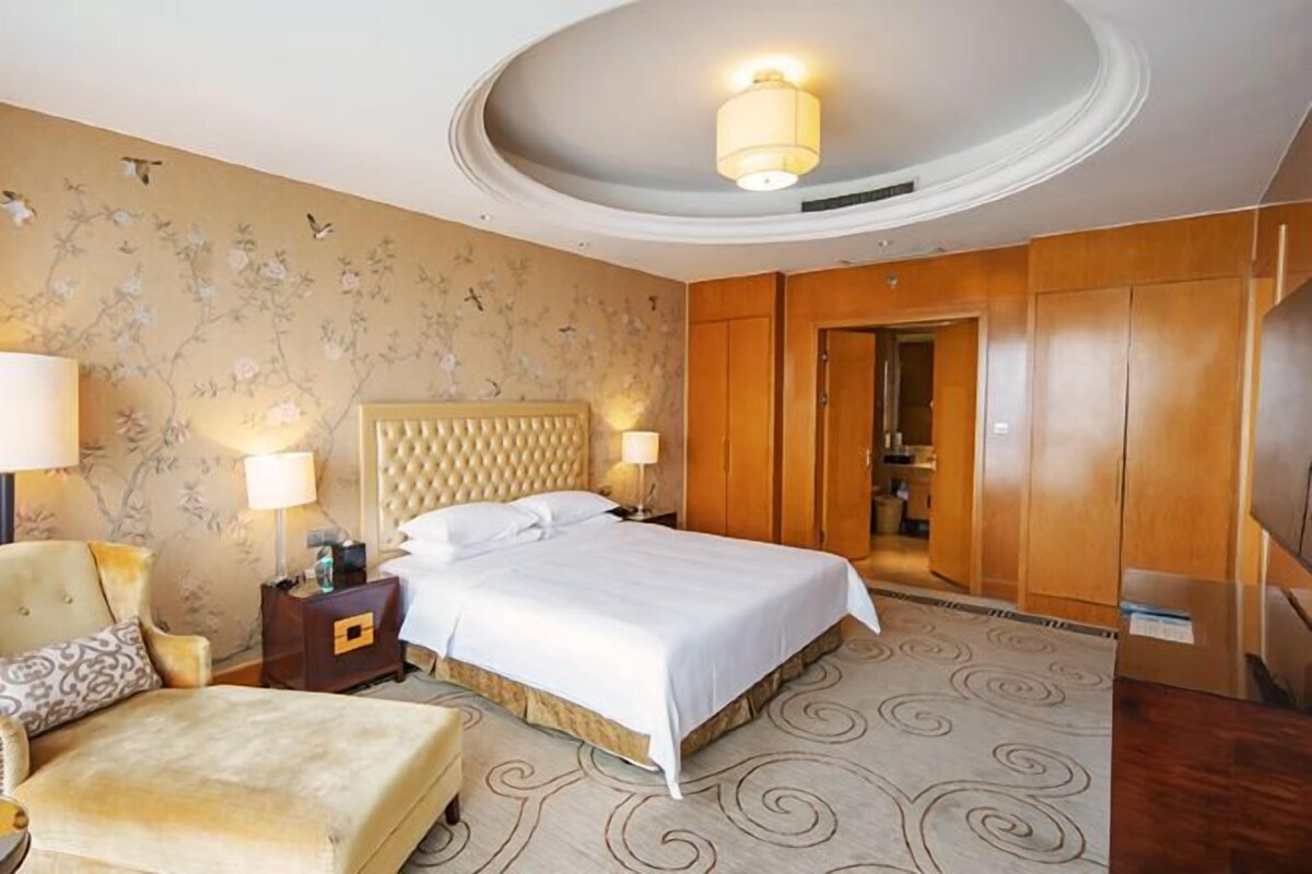 A hotel room with a large bed, a chair, a nightstand, and a wardrobe.