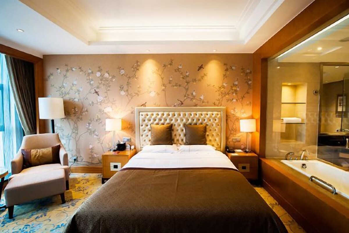 A hotel room with a large bed, a sitting area, a bathroom with a bathtub, and a large mirror.