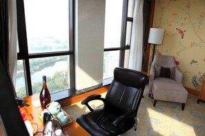 A room with a large window, a black office chair, a beige armchair, and a table with various items. - Binjiang International Hotel (Tengzhou)