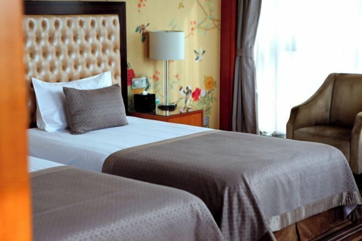 A hotel room with a tufted headboard, a bedside table with a lamp, and a floral wallpaper.