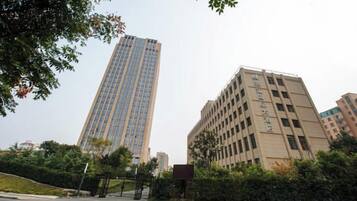 A tall building with a modern design, surrounded by greenery and other buildings.