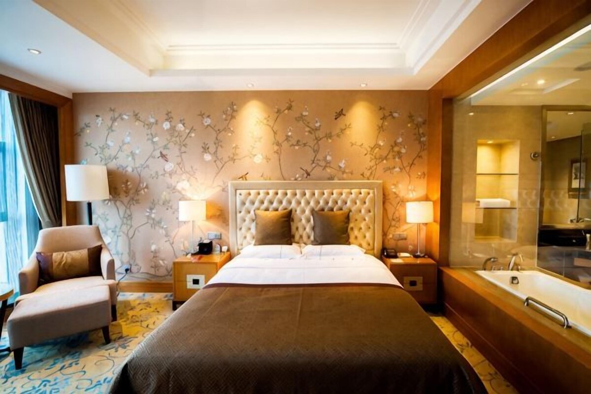A hotel room with a large bed, a sitting area, a bathroom with a bathtub, and a decorative wall.