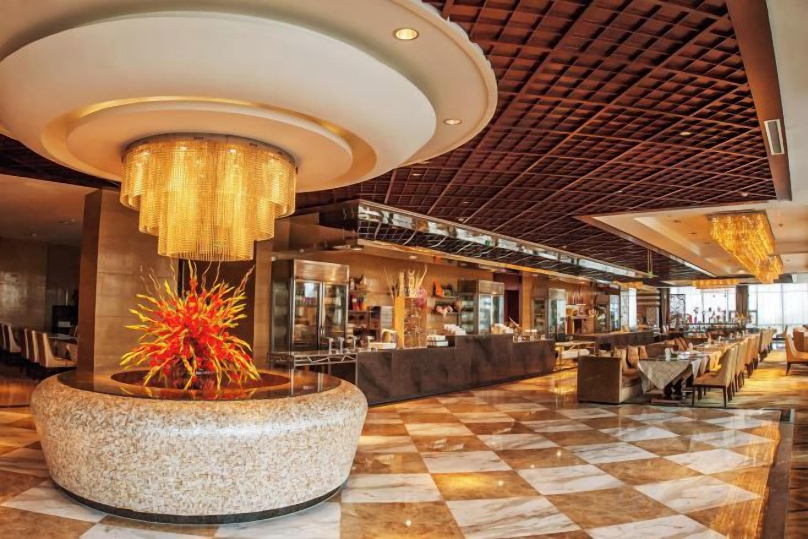 A spacious lobby with a checkered floor, a central decorative fountain, and a modern ceiling design.