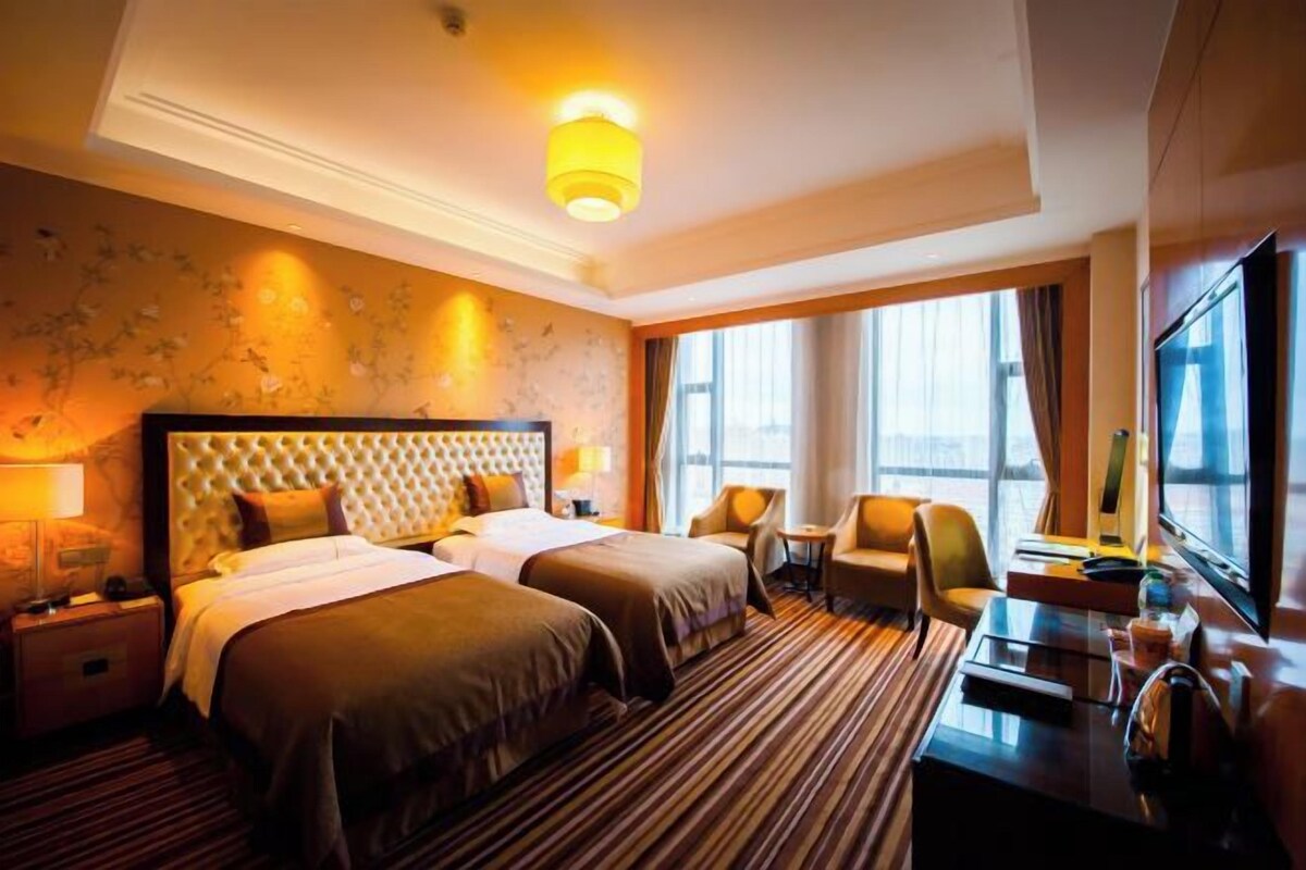 A hotel room with two beds, a desk, a chair, and a large window.
