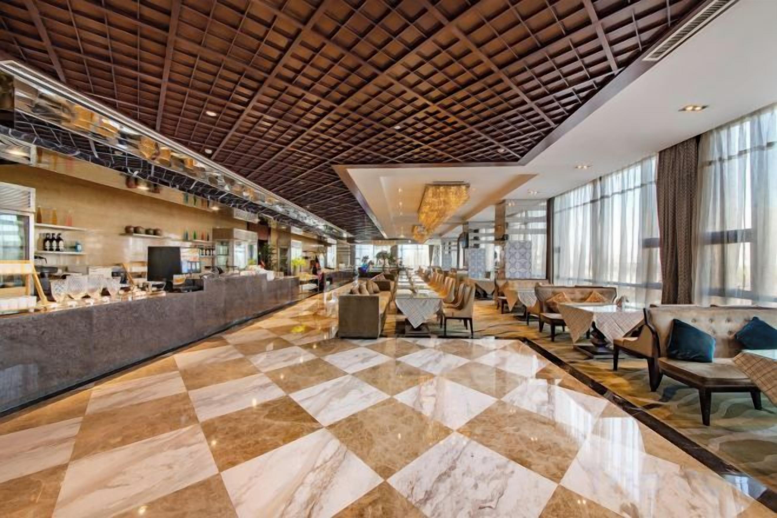 A spacious lobby with a checkered floor, a high ceiling with a wooden grid, and seating areas with tables and chairs.
