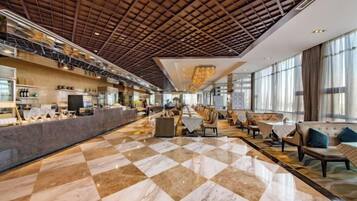 A spacious lobby with a checkered floor, a high ceiling with a wooden grid, and seating areas with tables and chairs.