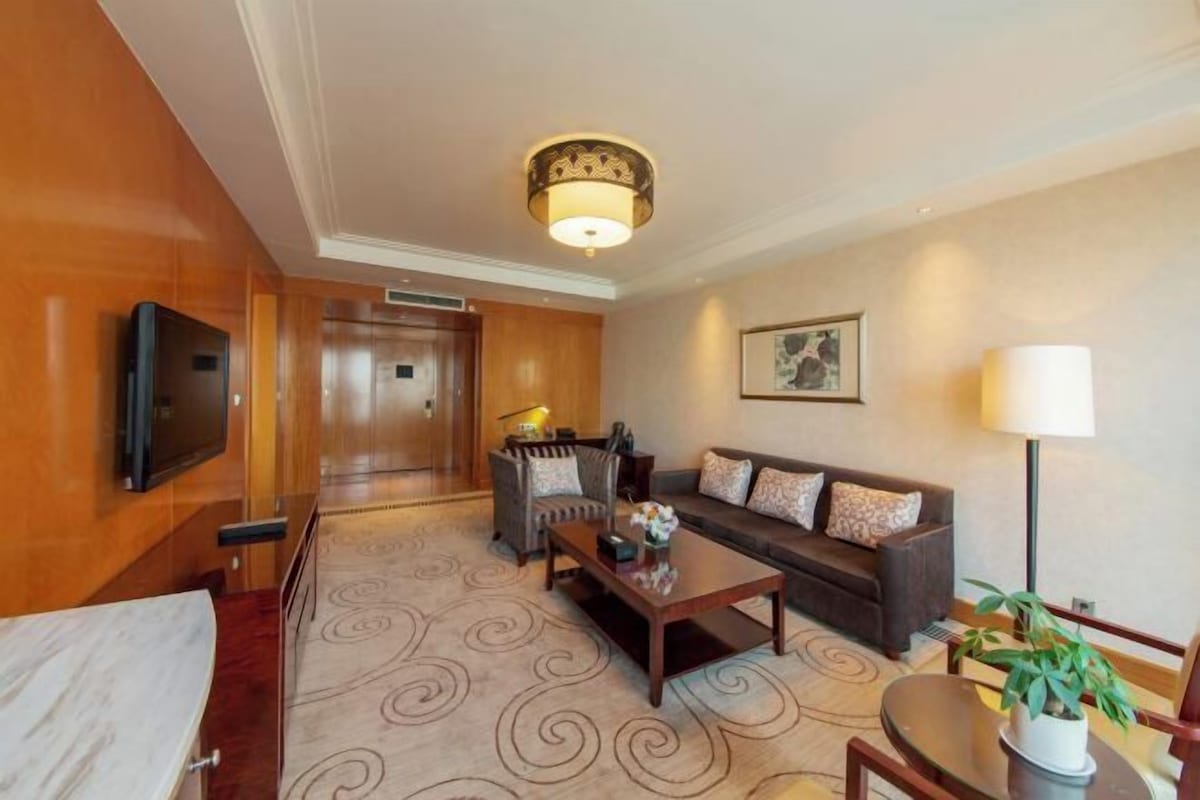 A hotel room with a sofa, a coffee table, a TV, a lamp, and a potted plant.