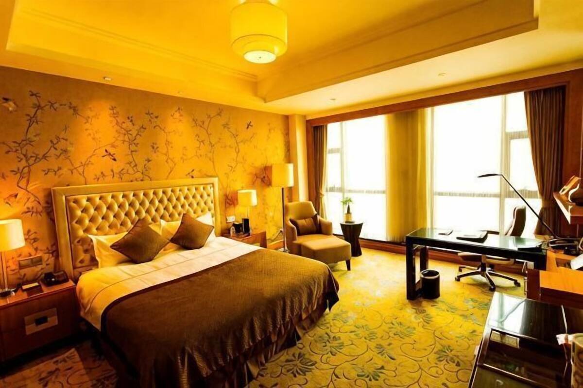 A hotel room with a large bed, a desk, a chair, and a window with curtains.