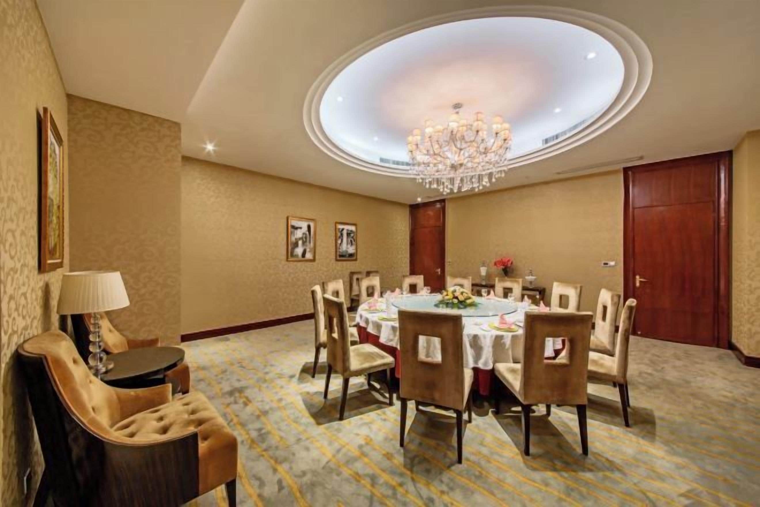 A conference room with a round table, chairs, a chandelier, and a carpeted floor.