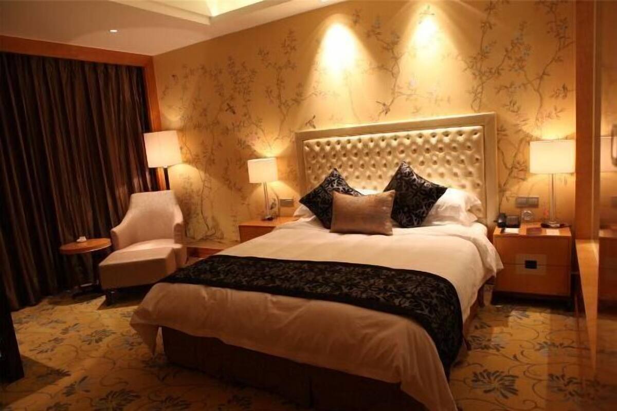 A hotel room with a large bed, two bedside tables, a chair, and a lamp.