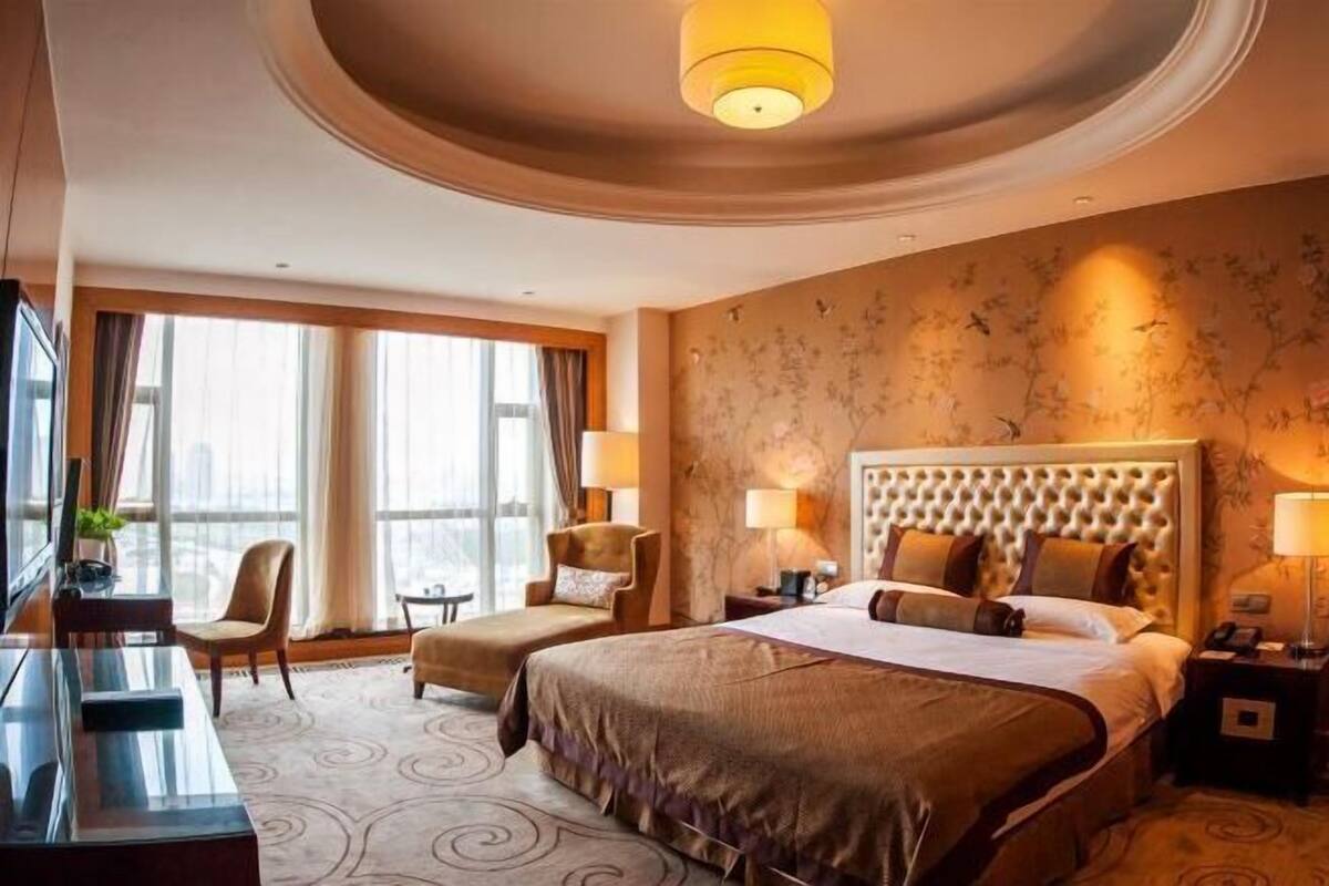 A hotel room with a large bed, two armchairs, a desk, and a television.