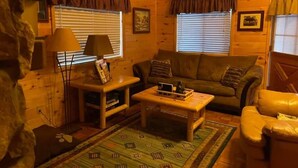 Ein gemütliches Blockhaus-Interieur mit Holzboden, einer Couch, einem Couchtisch und einer Lampe.