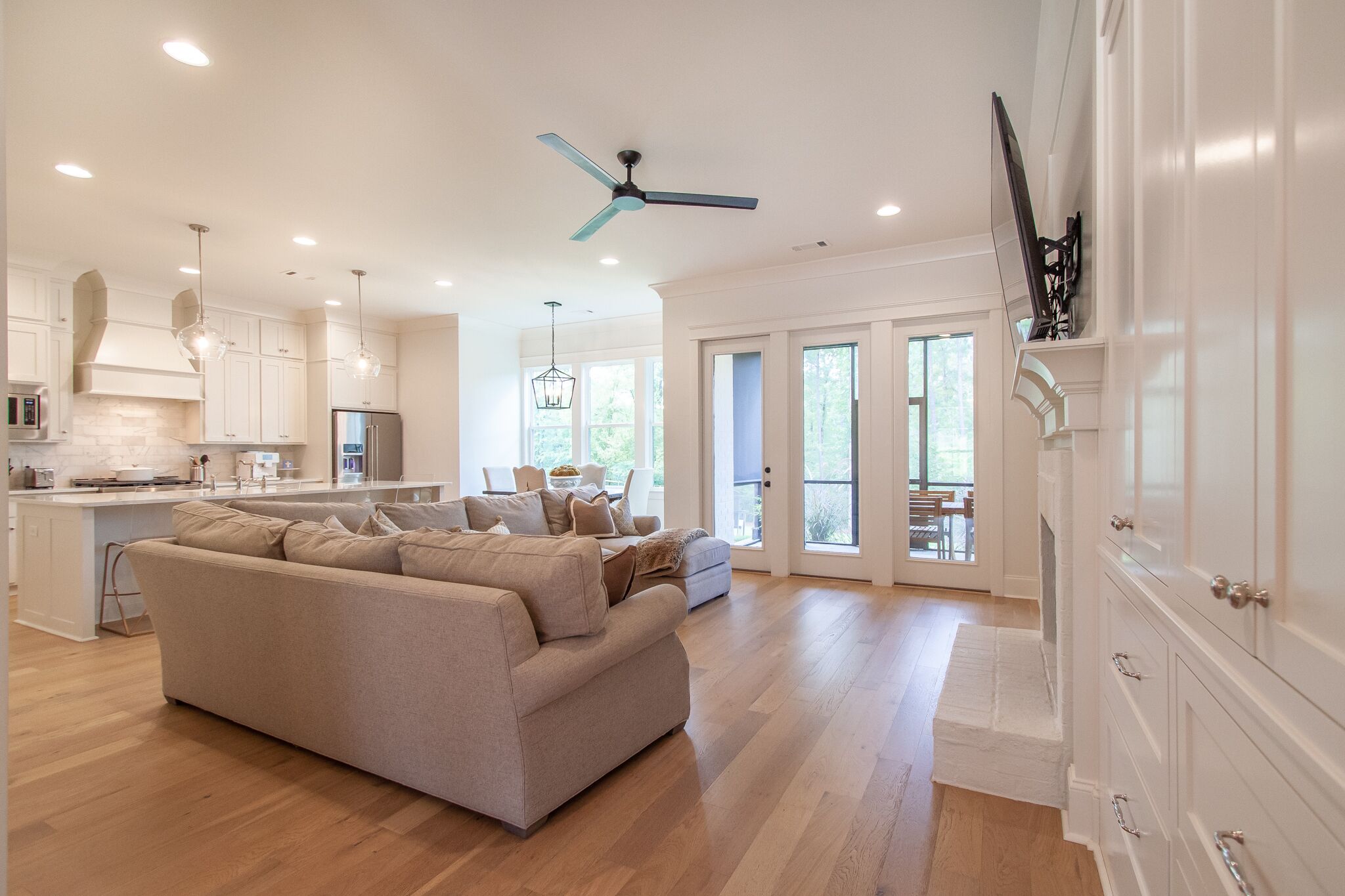 A spacious living area with a large beige sofa, a kitchen with white cabinetry, and a ceiling fan.