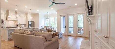 A spacious living area with a large beige sofa, a kitchen with white cabinetry, and a ceiling fan.