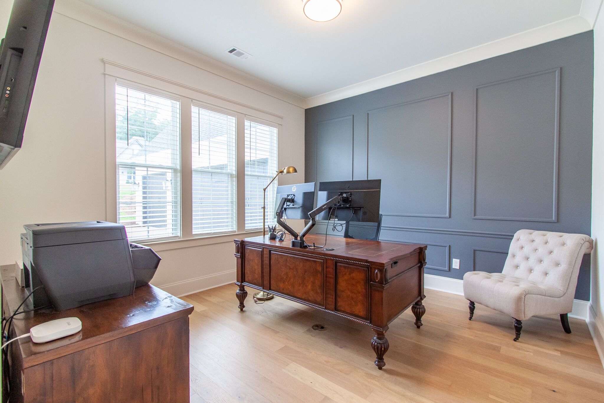 A room with a wooden desk, a chair, a printer, and a lamp.