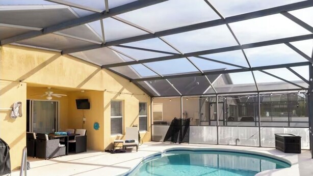 Une piscine extérieure couverte avec un toit en verre, un ventilateur de plafond et un téléviseur.