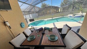 Une terrasse extérieure avec une table en bois, mise pour deux personnes, entourée de fauteuils confortables, donnant sur une piscine.