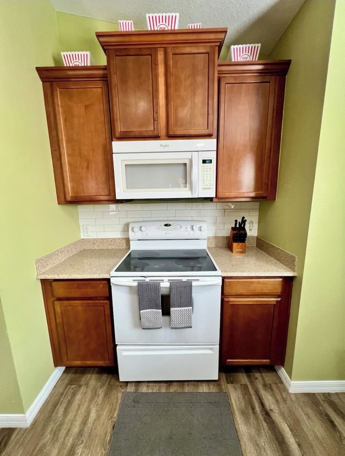 Una cocina con armarios de madera, un microondas blanco, una estufa y una encimera de granito.