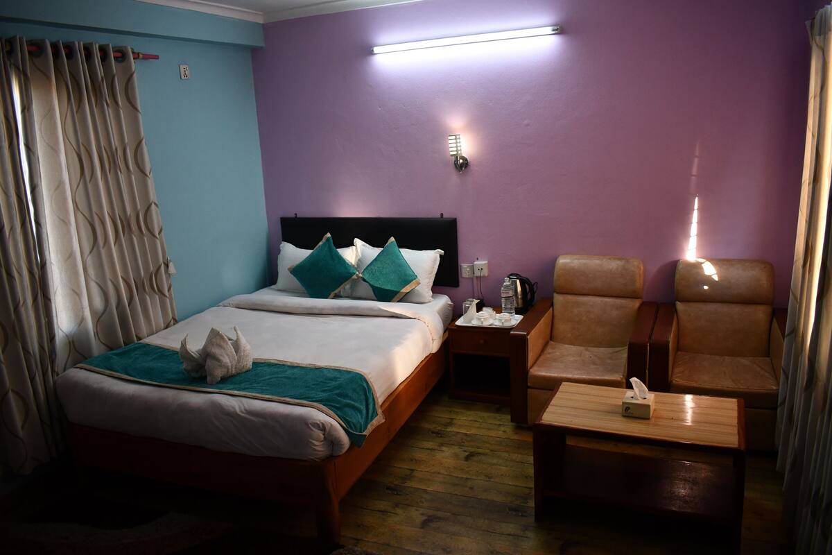 A hotel room with a bed, a nightstand, a chair, and a small table.
