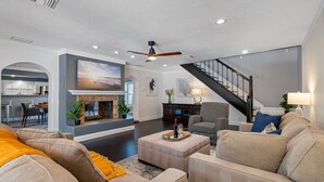 A spacious living room with a fireplace, a staircase, and a dining area visible through an archway. - Huge Luxury Heated Pool/Spa Villa w/ Game Room, Office, Exercise Area & More! (Tampa)