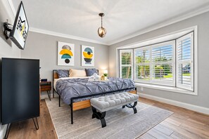 A bedroom with a bed, bedside tables, a TV, artwork, and a window with shutters. - Huge Luxury Heated Pool/Spa Villa w/ Game Room, Office, Exercise Area & More! (Tampa)