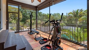 A balcony with exercise equipment, a wooden bench, and a view of a pool and greenery. - Huge Luxury Heated Pool/Spa Villa w/ Game Room, Office, Exercise Area & More! (Tampa)