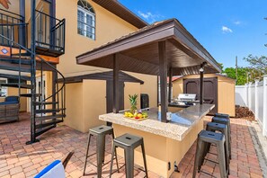 An outdoor kitchen area with a bar stool seating, a grill, and a fruit display.