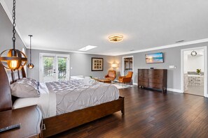A bedroom with a bed, two chairs, a dresser, and a TV on the wall.
