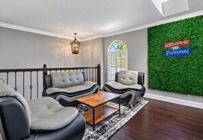 Una sala de estar moderna con un sofá, sillones, una mesa de centro y una pared decorativa con un letrero de neón.