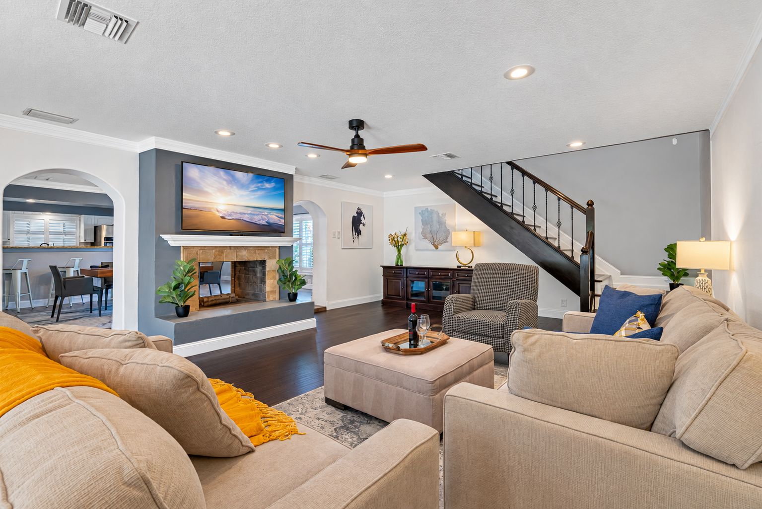 A spacious living room with a fireplace, a large flat-screen TV, a staircase, and a dining area.