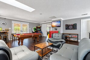 Ein Wohnzimmer mit Billardtisch, einer gemütlichen Sitzecke, einer Bar mit Flaschen und einem Fernseher.