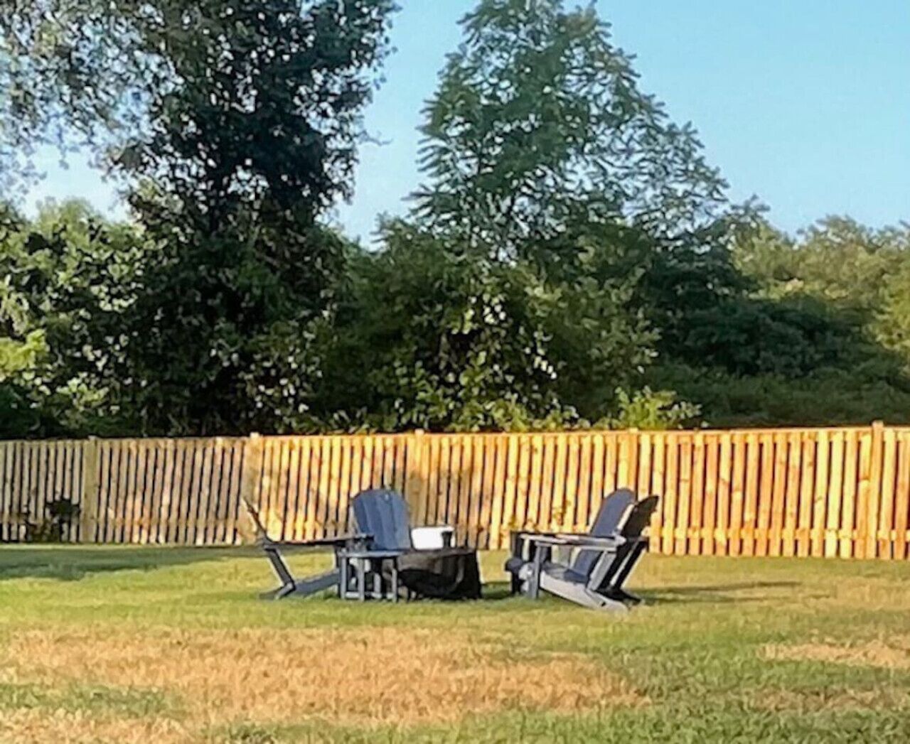 An outdoor seating area with two chairs and a table, surrounded by a wooden fence and trees.