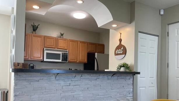 A kitchen with wooden cabinets, a stone backsplash, and a black countertop. There are two yellow chairs and a small table with a potted plant. - Cozy, bright 2BD w/yard, close to DT-bikes avail! (Manassas)