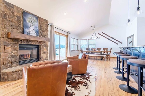 Uma sala de estar ampla com lareira de pedra, sofás de couro, tapete de couro bovino e uma área de jantar com móveis de madeira.