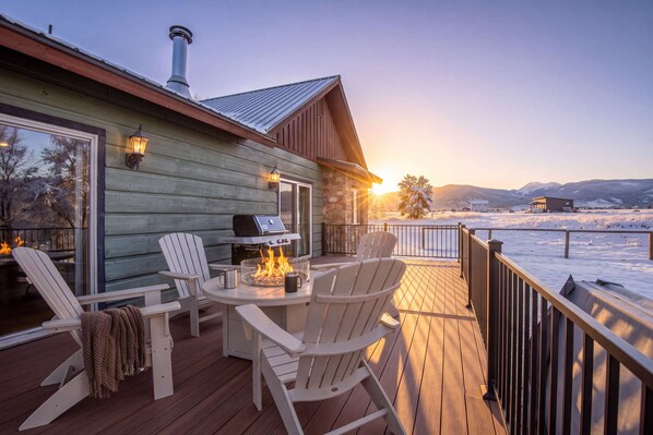 A wooden deck with outdoor seating and a grill, overlooking a snowy landscape.