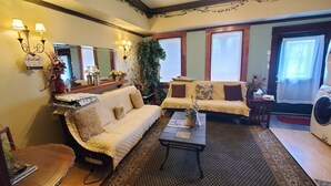 A cozy living room with a sofa, armchair, and coffee table, a washing machine, and a large mirror with wall sconces. - Downtown 1 Bedroom Duplex can Sleep 5 Close to Everything (Indianapolis)