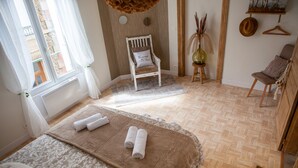 Una habitación con cama, una silla, un ventanal y una pequeña mesa con un jarrón.