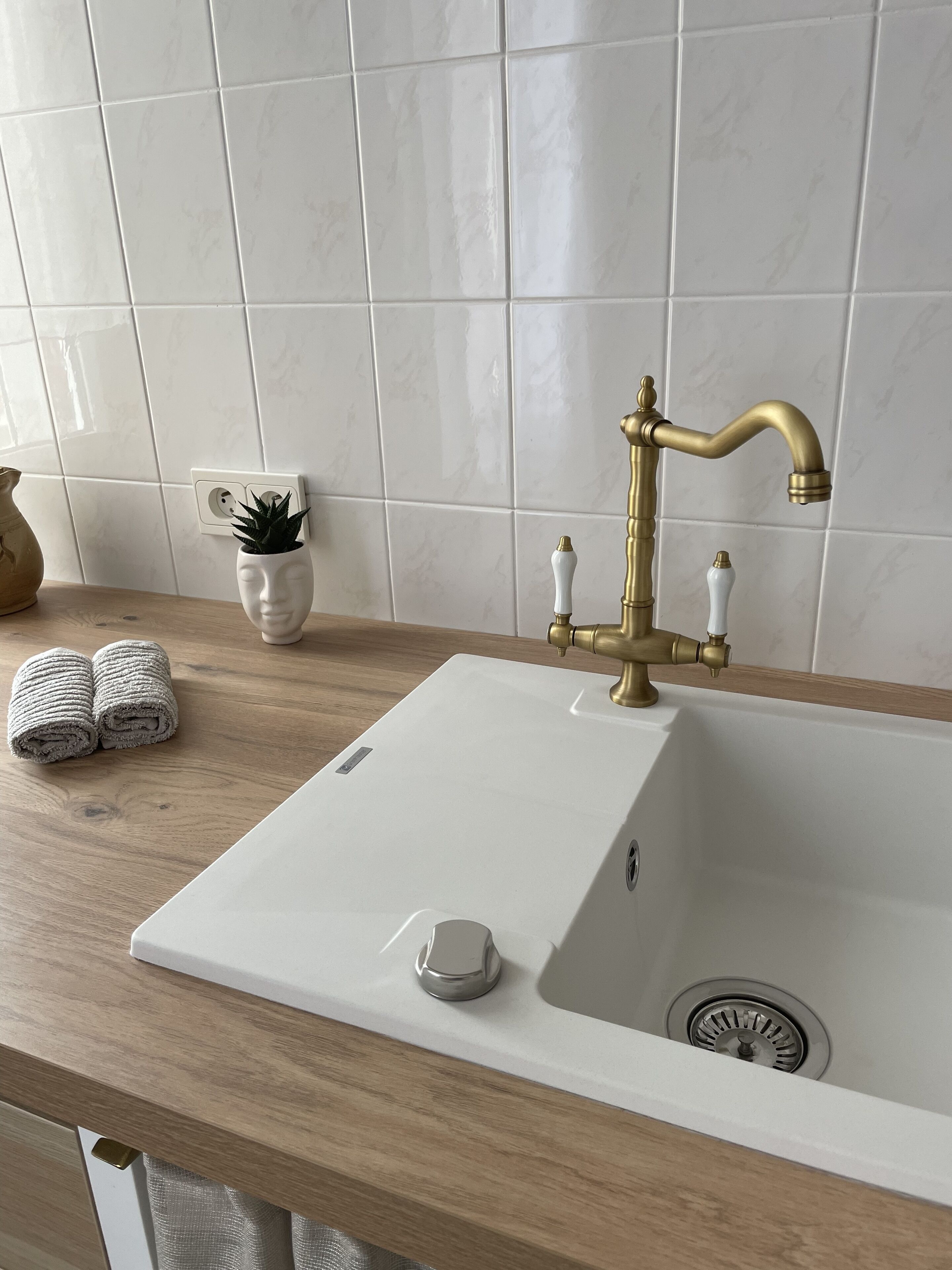 A bathroom with a white sink, brass faucet, and a wooden countertop.