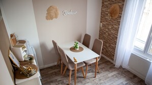 Un comedor con una mesa blanca, cuatro sillas, una planta pequeña y un adorno en la pared.