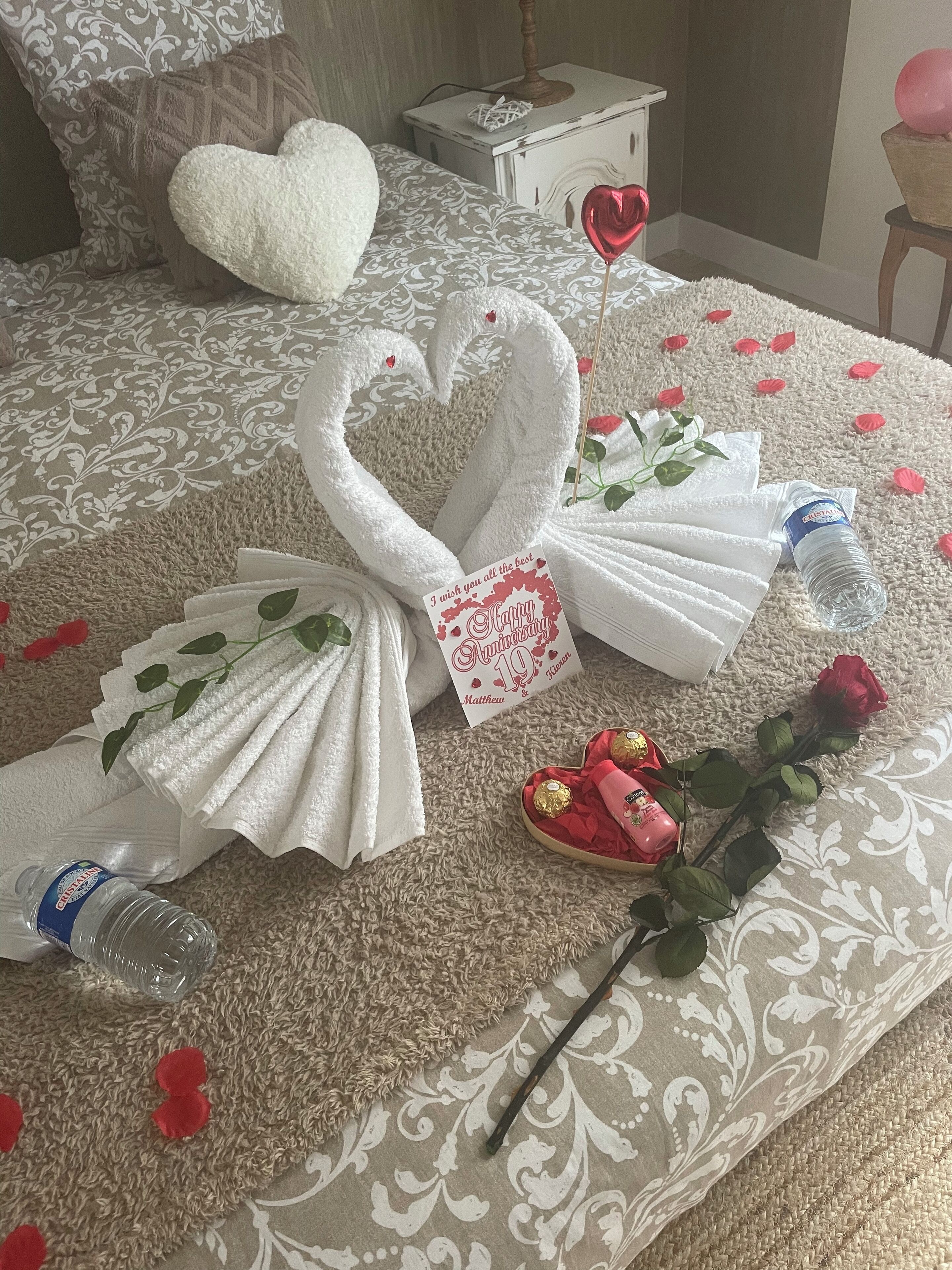 A bed with a decorative swan towel arrangement, a card, chocolates, and a rose.
