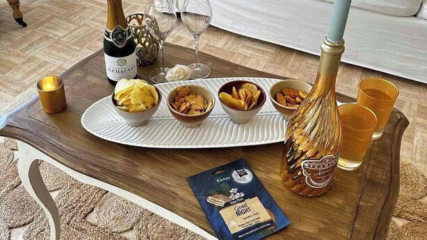 Una sala de estar con una mesa redonda para café, una botella de champán, copas y recipientes con aperitivos.